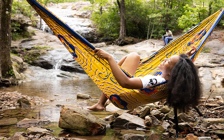 Girl sitting in a hammock over a stream. Visit outdoorafro.org